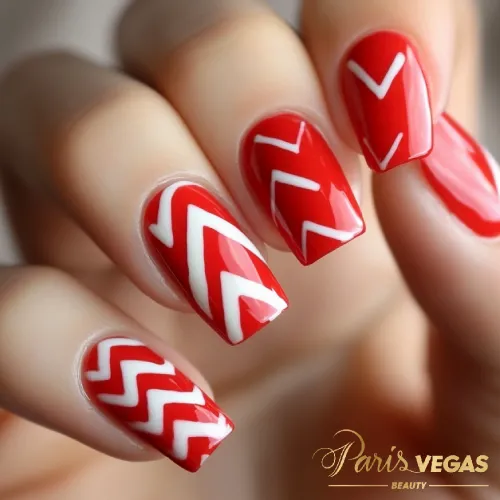 Decorações em unhas vermelhas com design chevron, criando um padrão geométrico moderno.