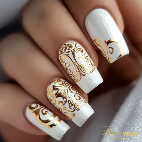 Unhas decoradas branco com arabescos dourados, criando um visual sofisticado e detalhado.