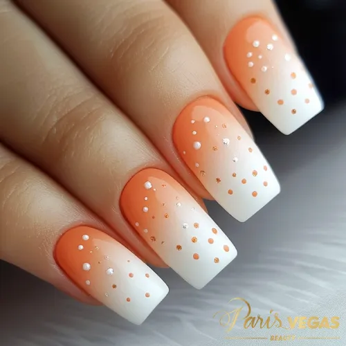 Unhas laranja com efeito degradê e detalhes em poá, destacando um design divertido e moderno.