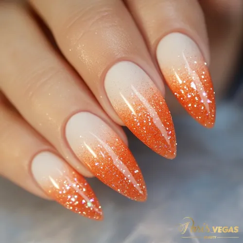 Unhas laranja com efeito ombré e glitter, destacando um design de manicure glamouroso.