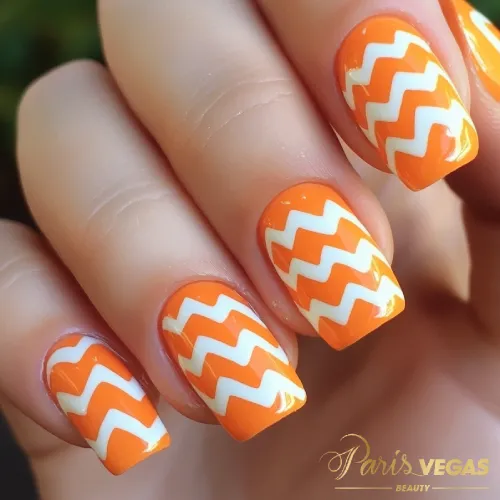 Unhas laranja com design chevron, destacando um estilo moderno e criativo.