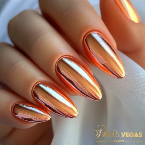 Unhas laranja em formato stiletto com esmalte metalizado, destacando um design ousado e moderno.