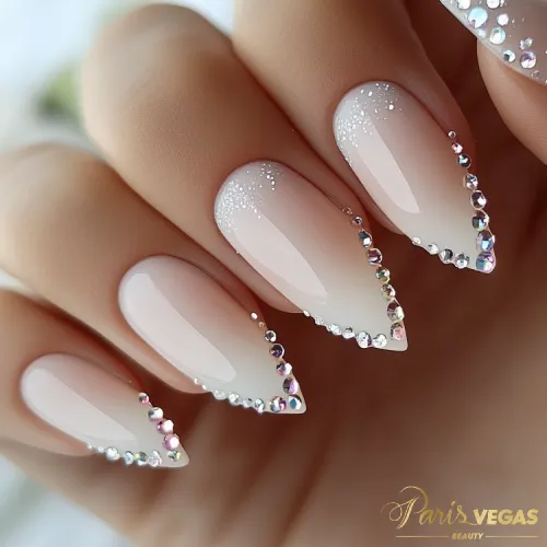 Unhas decoradas bege estilo stiletto com pedrarias, design sofisticado e glamouroso feito por manicure perto de você.