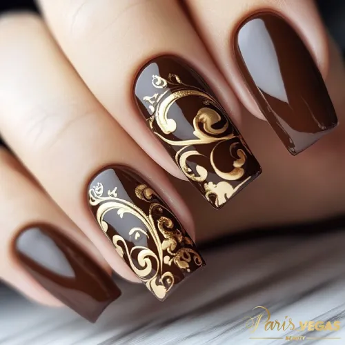 Detalhes de arabescos dourados em design de unhas marrons, mostrando elegância e sofisticação.