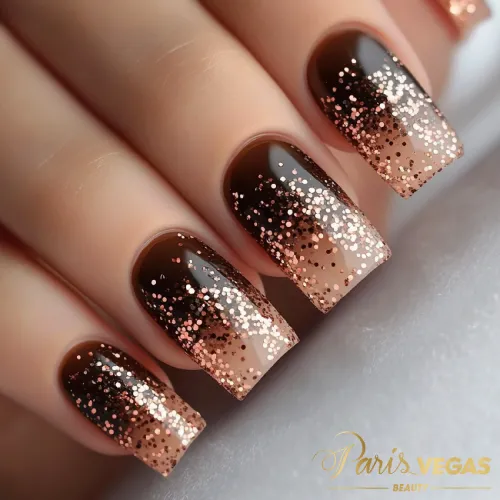 Unhas marrons com efeito degradê e detalhes em glitter, criando um design elegante e brilhante.