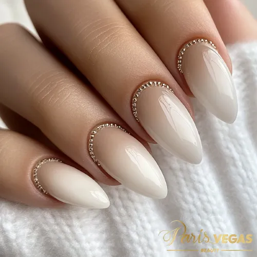 Unhas nude com efeito babyboomer e detalhes em metais, criando um visual sofisticado e moderno.